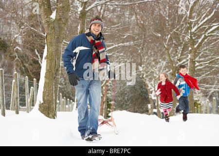 Vater Kinder auf Schlitten durch verschneite Winterlandschaft ziehen Stockfoto