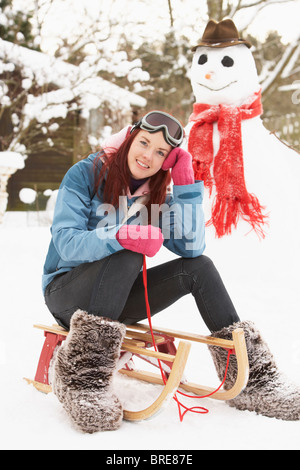 Teenager-Mädchen mit Schlitten neben Schneemann Stockfoto