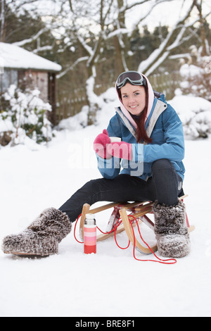 Teenager-Mädchen mit Schlitten neben Schneemann mit Kolben und Heißgetränk Stockfoto