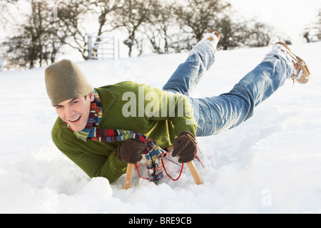 Junger Mann reitet auf Schlitten In Schneelandschaft Stockfoto