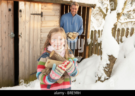 Vater und Tochter sammeln Protokolle aus Holz laden im Schnee Stockfoto