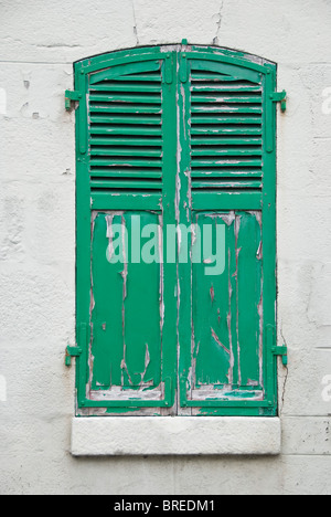 Ein Fenster mit geschlossenen grünen Fensterläden und abblätternder verwitterter Farbe, Frankreich Stockfoto