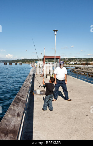 friedliche Szene auf menschenleeren Edmonds Angelpier steht wie kleine asiatische junge seine Rute & Opa wirft zu beraten Stockfoto