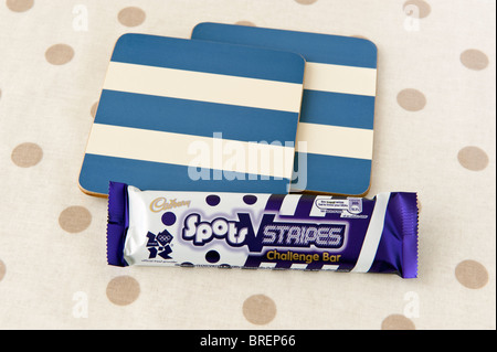 Cadbury Flecken und Streifen Choc-Bar und 2 Blau-Creme gestreiften Untersetzer auf einer Creme und braun gefleckten Matte Stockfoto