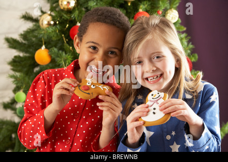 Zwei junge Kinder essen Weihnachtsplätzchen vor Weihnachtsbaum Stockfoto