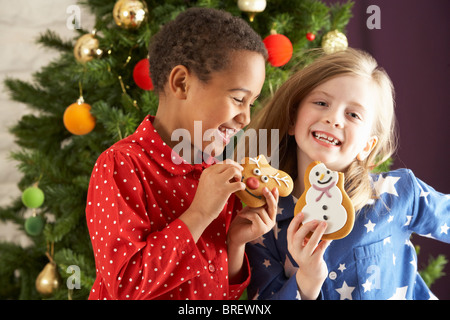 Zwei junge Kinder essen Weihnachtsplätzchen vor Weihnachtsbaum Stockfoto