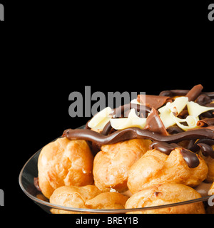 Schüssel mit Profiteroles erstickt in Schokolade, isoliert gegen einen schwarzen Hintergrund mit Textfreiraum Stockfoto