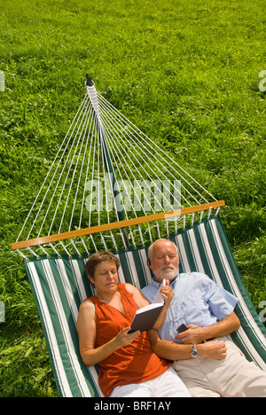 Älteres paar liegen in der Hängematte, Mann ein Buch lesen, Frau Musikhören Stockfoto