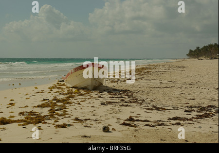 Verwitterte Boot mit abblätternde Farbe an windigen Sandstrand in Tulum Mexico.Biosphere in Ferne mit flauschigen Wolken bilden gebunden Stockfoto