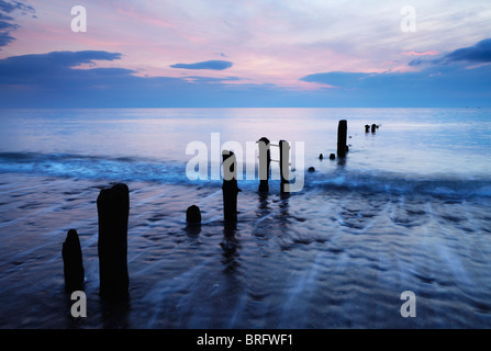 Kühle Töne Leuchten Whitbys Strand mit Wellen rund um die Buhnen Stockfoto