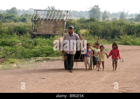 Eine Gruppe von jungen Kindern sind Fuß mit einem Landwirt, als er auf einem Feldweg in Kratie, Kambodscha geht. Stockfoto