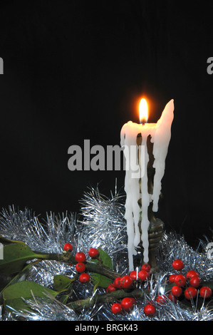 Eine brennende Kerze tropft mit Wachs, umgeben von Lametta und Holly Beeren zu Weihnachten. Dorset, UK Dezember 2008 Stockfoto