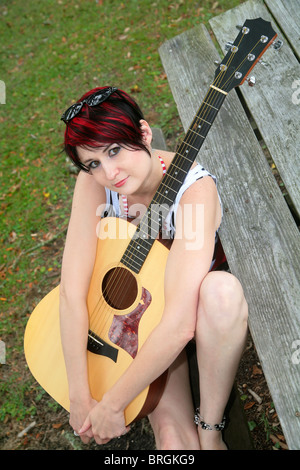 eine rothaarige Frau hält eine Gitarre im Freien auf einem Picknick Tisch Bank Stockfoto