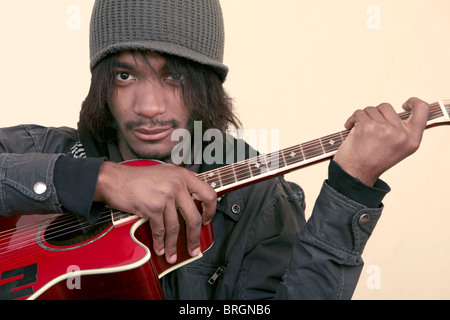 ein afrikanischer Amerikaner junger Mann hält eine rote Gitarre auf einem gelben Hintergrund Stockfoto
