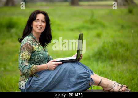 Frau sitzt auf der Bank mit Laptop im park Stockfoto