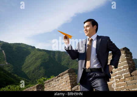 Geschäftsmann auf der chinesischen Mauer hält Papierflieger Stockfoto