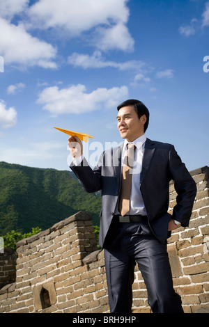 Geschäftsmann auf der chinesischen Mauer hält Papierflieger Stockfoto