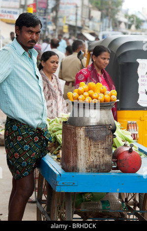 Indischer Mann Straßenhändler verkaufen gekocht Maiskolben. Puttaparthi, Andhra Pradesh, Indien