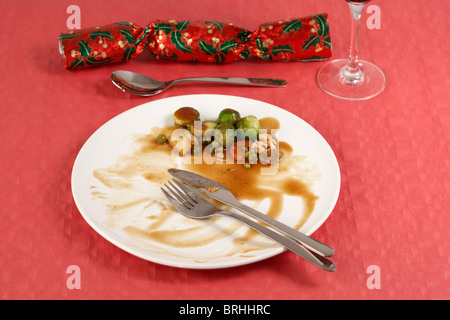 fertige Weihnachtsessen mit Sprossen links auf weißem Teller auf roten Tischdecke Christmas cracker Stockfoto