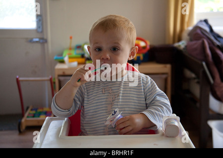 Junge 16 Monate alt einen messily Essen Joghurt essen. Hampshire, England. Stockfoto