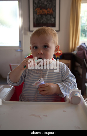 Junge 16 Monate alt einen messily Essen Joghurt essen. Hampshire, England. Stockfoto