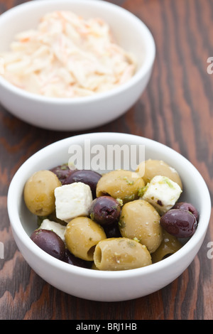 Vorspeise von Grün und Kalmata Oliven mit Feta-Käse in einer weißen Schüssel mit Krautsalat im Hintergrund Stockfoto