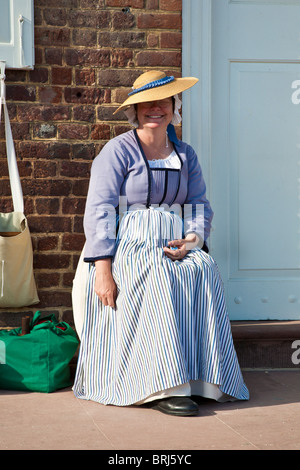 Lächelnde Frau in zeitgenössischer Kleidung gekleidet sitzt vor Haustür in Colonial Williamsburg, ein lebendiges Geschichtsmuseum in Williamsburg, VA Stockfoto