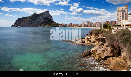 Playa La Fossa, mit Felsen und verführerisch transparentes Wasser plus Promenade, Strand und auf dem Hintergrund der riesigen Felsen von Ifach. Stockfoto