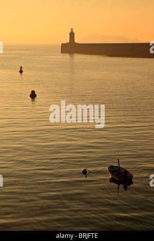 Vor Sonnenaufgang leuchtet St Peter Port Leuchtturm in Guernsey mit der Insel Herm Silhouette am Horizont Stockfoto