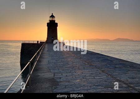 Sunrise leuchtet St Peter Port Leuchtturm in Guernsey mit der Insel Herm Silhouette am Horizont Stockfoto