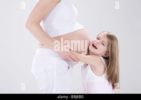 Kleine Mädchen umarmt schwangere Mutter Stockfoto