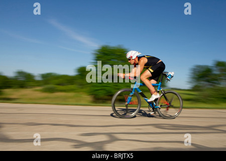 Ein männlicher Athlet Training für einen Triathlon an einem See mit dem Fahrrad. Stockfoto