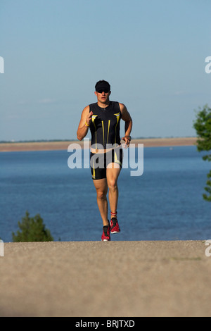 Eine männliche Athlet läuft beim Training für einen Triathlon an einem See. Stockfoto