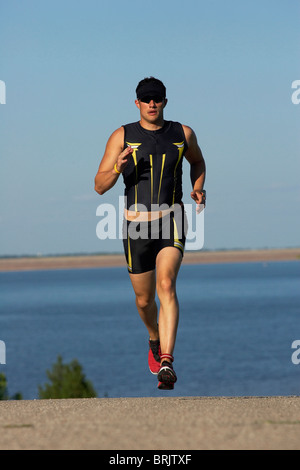 Eine männliche Athlet läuft beim Training für einen Triathlon an einem See. Stockfoto