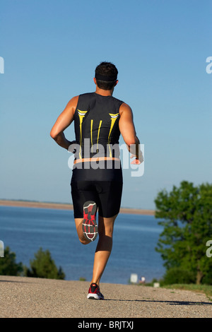 Eine männliche Athlet läuft beim Training für einen Triathlon an einem See. Stockfoto