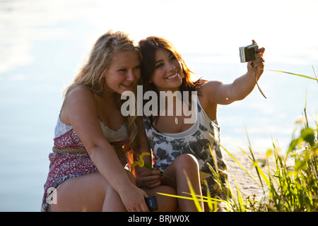 Zwei junge Frauen Lächeln während der Einnahme ein Bild von sich selbst an einem sonnigen Tag am See. Stockfoto