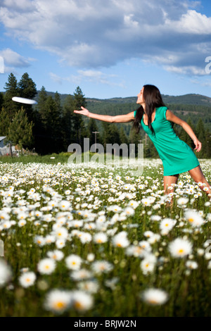 Eine schöne junge Frau lächelt während Threwing einen Frisbee in einem Feld von wilden Blumen. Stockfoto