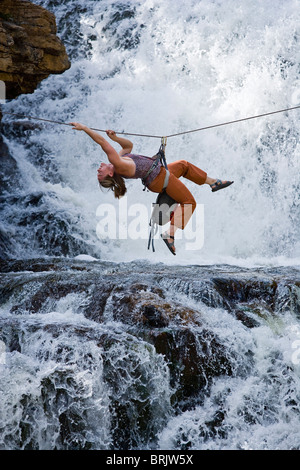 Eine Frau kreuzt einen Wasserfall mit einer Hilfsseilbahn auf einem Seil. Stockfoto