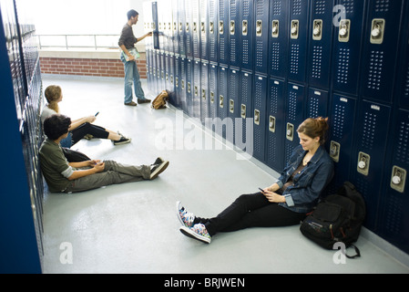 Schülerinnen und Schüler sitzen auf Boden von Schließfächern, die Nutzung von Mobiltelefonen Stockfoto