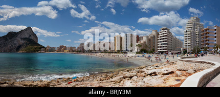 Panoramablick auf Playa La Fosa, mit Felsen und verführerisch transparentes Wasser, Promenade, Strand und Felsen von Ifach im Hintergrund Stockfoto