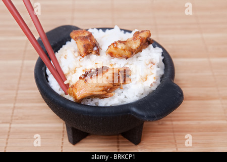 eine Schüssel mit hausgemachten gesunde Sesam Huhn auf weißem Reis mit Stäbchen in einer schwarzen Schale Stockfoto