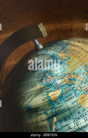 Ein kleiner Vintage Globus des Planeten Erde, Hervorhebung der UK und Westeuropa, mit einem antiken Kartenhintergrund. Stockfoto