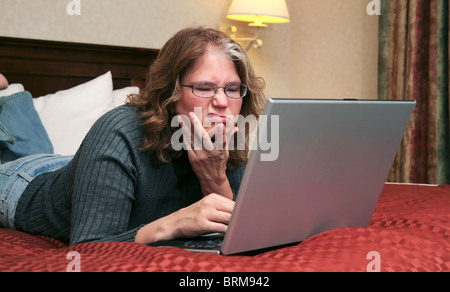 ein 40er Frau sah verwirrt oder unglücklich auf ihrem Laptop beim liegen im Bett Stockfoto