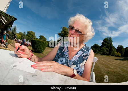 Ältere Frau sitzen im freien schreiben eine Postkarte an einem heißen Sommertag. Stockfoto