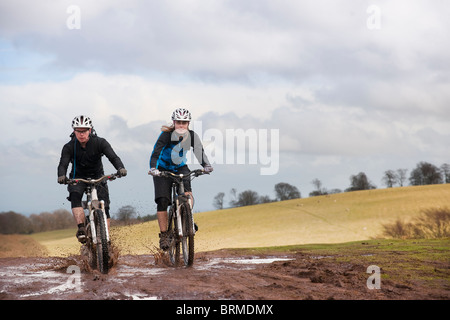 Paar Reiten Fahrrad durch schlammigen Pfützen Stockfoto