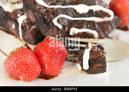 einen kleinen Bissen genommen aus zwei frischen, köstlichen Schokoladen-Brownies auf einem weißen Teller mit frischen Erdbeeren Closeup Winkel suchen Stockfoto