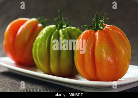 Drei rote und grüne Tomaten auf grauem Hintergrund Stockfoto