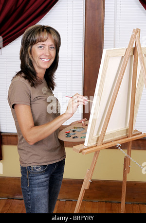 eine Frau, die beim Malen eines Bildes auf ihrem weißen Leinwand lächelnd Stockfoto