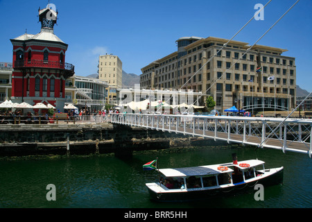 Victoria und Alfred Waterfront mit dem Uhrturm und ein Touristenboot unter einer Brücke Stockfoto