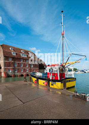 Gelbe kommerziellen Shell Fischkutter vertäut Kai am Ashlett am Southampton Water mit alten Mühle rote Backsteingebäude Stockfoto